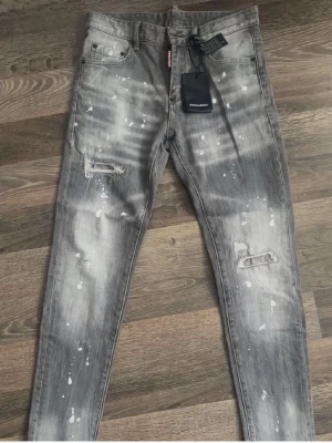 Dsquered 2 Jeans  - Säljer ett par grå  jeans från Dsquared2 med coolt slitna detaljer, färgstänk och trasiga partier vid knäna.  Helt nya aldrig använda. Pris kan diskuteras 