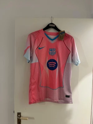 Barca x Nike rosa matchtröja - Säljer en Barcelona matchtröja från Nike i en riktigt snygg rosa och ljusblå färgkombination. Tröjan har korta ärmar, klubbmärke och Nike-logga på bröstet samt Spotify-logga i mitten. Tillverkad i lätt polyester med ventilerande meshpaneler. Tillgänglig i storlek S-M-L