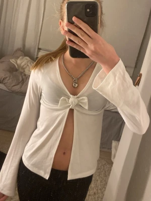 Söt vit topp - Säljer en trendig vit långärmad topp från H&M med v-ringning och snygg knytrosett framtill. Toppen har en snygg öppen detalj under bysten. Perfekt till både vardag och fest💕Säljer då den är för liten för mig!