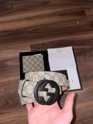 GG beige GG-mönstrat bälte och plånbok storlek 105cm - GLÖMDE PÅ BILDERNA MEN HAR OCKSÅ GG PÅSE SOM KOMMER MED DM FÖR BILDER!   Säljer ett snyggt GG-bälte och GG-plånbok i ett set båda är beige med klassiskt GG-mönster och en stor svart rund spänne med GG-logga. Bältet är tillverkat i skinn och har en lyxig känsla, perfekt för att lyfta din outfit. Kommer med originalförpackning och kvitto. 