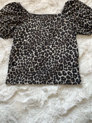 Leopardmönstrad topp från H&M - Säljer en leopardmönstrad topp från H&M med puffiga korta ärmar. Toppen har fyrkantig halsringning och är gjord i ett mjukt, stretchigt material. Färgerna går i beige, svart och brunt och den har en riktigt trendig vibe. Pris 20kr