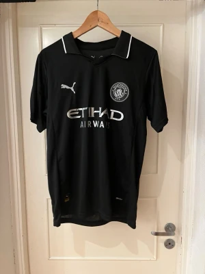Manchester city 26/26 home kit X Cherki 10 - Säljer en svart Manchester City tröja från Puma i storlek M. Tröjan har vita detaljer, klassisk krage och tryck med Etihad Airways på bröstet. På ryggen står det CHERKI och nummer 10 i vitt. Materialet är lätt polyester och har RE:FIBRE-teknologi.