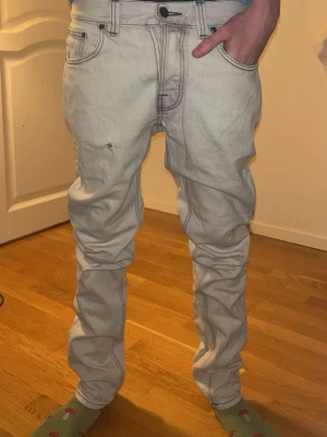 Nudie Jeans - Säljer ett par vita jeans med raka ben och klassiska fem fickor. Jeansen har kontrastsömmar och snygga detaljer på bakfickorna. Passformen är normal och materialet är klassisk denim. Perfekta för dig som gillar en clean och enkel stil.