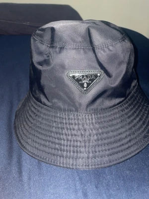 Svart bucket hat från Prada - Säljer en svart bucket hat från Prada med klassisk logga framtill. Hatten är oanvänd 
