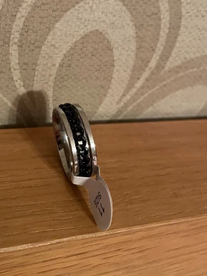 Fidgetring - Fidgetring i rostfritt stål Silverfärgad med svart kedjemönstrad rörlig innerdel.  St 11 vilket motsvarar ca 20,6 mm  Oanvänd