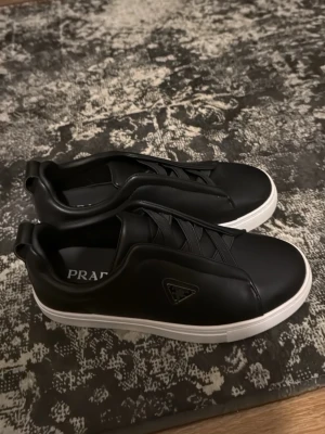 Svarta sneakers  strl 38 - Säljer ett par stilrena svarta sneakers i storlek 38. Skorna har en vit platt sula. Nya, endast testade. Passar killar och tjejer.  Laceless riktigt fina