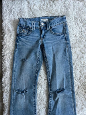 Ljusblå jeans Gina Tricot 152 - Ljusblå jeans från Gina Tricot i storlek 152 med slitna detaljer på benen och klassisk femficksmodell. Jeansen har raka ben och dubbla silverknappar i midjan. Perfekta för en avslappnad och trendig look. Har gjort hålen själv❣️❣️