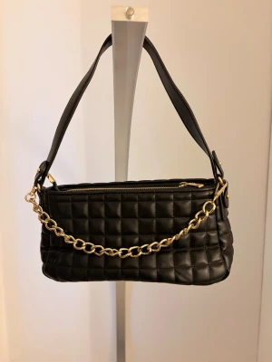 Svart axelväska med kedja - En svart quiltad axelväska med guldfärgad kedjedetalj. 