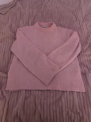 Ljusrosa stickad tröja Kappahl - Mysig ljusrosa stickad tröja från Kappahl med ribbade muddar vid ärmslut, halsringning och nederkant. Tröjan har en klassisk rak passform och är perfekt för kyligare dagar. Enkel att matcha med jeans eller kjol.