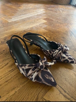 Leopardmönstrade pumps med rosett - Säljer ett par snygga pumps med leopardmönster och spetsig tå. Skorna har en liten klack, öppen häl med smal rem och en stor rosett framtill. Aldrig använda så i jättebra skick. 