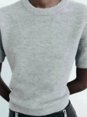 Grå stickad kortärmad tröja från Zara - Mysig grå stickad tröja från Zara med korta ärmar och rund hals. Tröjan har ribbade muddar vid hals, ärmslut och nederkant. Perfekt att styla med jeans eller kjol för en chill look. Säljer då jag aldrig använder den!