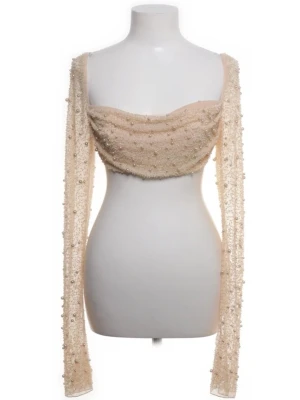 Beige mesh topp med pärlor - Supersnygg croppad mesh topp i beige med långa ärmar och massor av pärlor över hela tyget. Toppen har en draperad byst, perfekt för att sticka ut på festen.