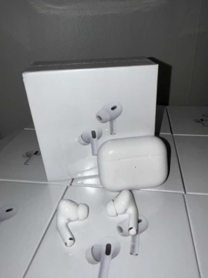 AirPods Pro 2 - Apple AirPods Pro med trådlös laddningsetui. Aktiv brusreducering, transparensläge och bekväm passform med silikonproppar. Fodralet och hörlurarna ser ut att vara i gott skick, endast mindre spår av användning syns. Perfekt för musik, samtal och träning.