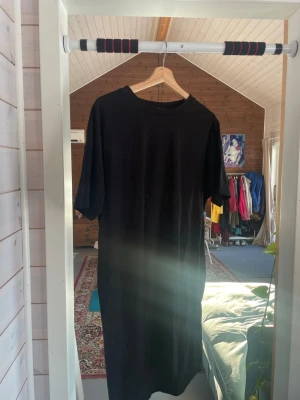 Svart T-shirtklänning - Enkel och stilren svart klänning från Amisu i t-shirtmodell. Klänningen har rund halsringning och korta ärmar. Tillverkad i mjukt material. Storlek EU 38 men skulle säga snarare XL.