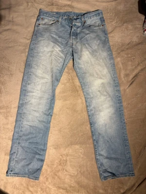 Levi's 501 ljusblå jeans W32 L32 - Klassiska Levi's 501 jeans i ljusblå tvätt med raka ben och femficksmodell. Jeansen har hög midja, knappgylf och tydliga kontrastsömmar. Tillverkade i slitstarkt bomullsjeans, perfekt för en avslappnad och tidlös stil.
