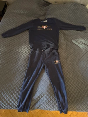 Marinblå mjukisbyxor & sweetshirt från GANT - Säljer ett GANT kit med marinblåa mjukisbyxor och sweetshirt med hög kvalité. Perfekta för chill dagar eller när du vill vara bekväm men ändå se snygg ut. Byxorna är i storlek Large med 43cm i bredd vid midjan och 105cm i längd. Tröjan är bredd 45cm mellan axlarna och 70cm i längd.