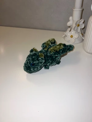 Mörkgrön bäbisdrake med limegröna detaljer💚 - Denna urgulliga bäbisdrake vill hitta sitt nya hem🐉💚Den har hårda blåa ögon💙 Den är ungefär likas stor som min handflata🐉 så cirka 15cm långa💚 Vikrad med massa kärlek, med mjukt garn från Rusta💚💚
