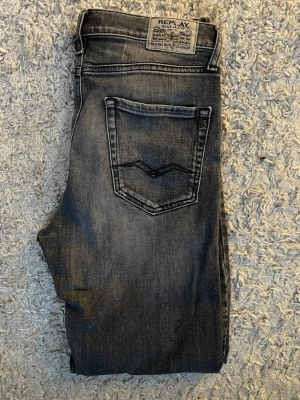Svarta Replay jeans  - Säljer ett par svarta jeans från Replay med snygg tvättad look och raka ben. Klassisk femficksmodell med tydliga sömmar och Replay-märke bak i midjan. Jeansen är i jeansmaterial och har en cool, lite sliten finish. Och är i st w26