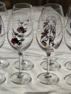 Kosta Boda vinglas med konstmotiv - Unika vinglas från Kosta Boda med coola illustrationer av ansikten i svart, blått, brunt och orange. Glasen har olika former och motiv, vissa med färgklickar och andra med stilrena linjeteckningar. Perfekta för att ge dukningen en personlig touch.