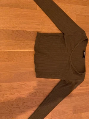 Olivgrön ribbad topp från FB Sister - Säljer en olivgrön croppad topp från FB Sister i storlek XS. Toppen har lång ärm, v-ringning och är ribbad i materialet vilket ger en snygg struktur. Perfekt till jeans eller kjol.