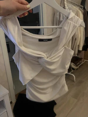Vit omlott topp från Bik Bok INTRESSEKOLL - Säljer en vit omlott topp från Bik Bok i storlek M. Toppen har en snygg draperad design med twistad detalj framtill och breda axelband. Materialet känns mjukt och stretchigt, perfekt för att skapa en cool och trendig look.