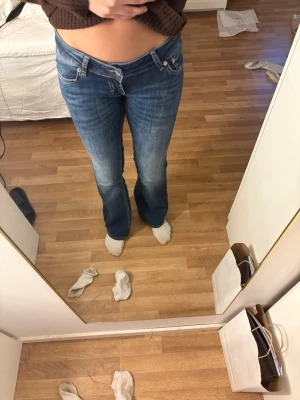 Blå bootcut jeans med låg midja - Säljer ett par klassiska blå bootcut jeans med snygg tvätt och låg midja. Jeansen har fem fickor, dragkedja och knapp framtill. Perfekta för dig som gillar en retro vibe och vill ha ett par jeans med lite utsvängda ben. Köpta för 400 använda 3 ggr