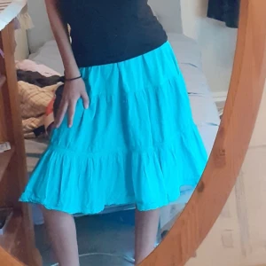 Turkos volangkjol i bomull - Säljer en unik turkos kjol med spets o volanger detaljer. Kjolen har avslappnad passform. Dessutom en luftig känsla och är gjord i mjukt bomullstyg. Perfekt för dig som gillar färg, tidig 2000 tal och vill ha något bekvämt och snyggt till sommaren. 