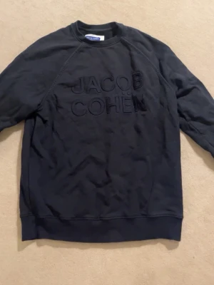 Svart sweatshirt från Jacob Cohën - Otroligt snygg och fräsch sweatshirt från Jacob Cohën som säljs i toppen skick. Den är använd sparsamt vid få tillfällen och även köpt i butik, storlek L men sitter som en M. Ser lite skrynklig ut då den är nytvättad, nypris är ca. 4500