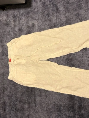 Beige linnebyxor med snörning - Säljer ett par ljusbeige linnebyxor med avslappnad passform och dragsko i midjan. Perfekta för varma dagar och riktigt sköna att ha på sig. Byxorna har elastisk midja och raka ben för en chill vibe.