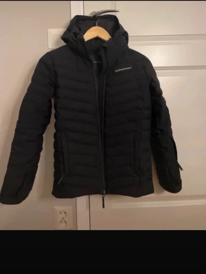 Peak performance jacka - Säljer en svart dunjacka från Peak Performance med huva och dragkedja framtill. Jackan har en quiltad design och två fickor med dragkedja. Perfekt för kalla dagar och riktigt snygg till alla outfits. Köpt för drygt 200. Barnstorlek. Perfekt som skidjacka