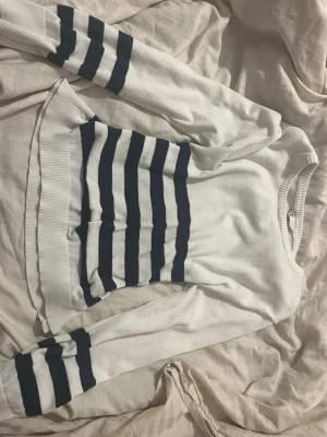 Vit och marinblå randig stickad tröja  - Säljer en vit stickad tröja från Cubus i storlek S med breda marinblå ränder på både mage och ärmar. Tröjan har rund halsringning, ribbade muddar och lång ärm. Perfekt för dig som gillar klassisk och enkel stil.