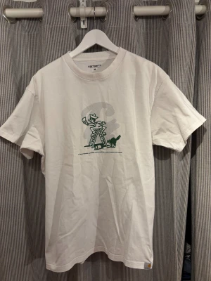 Vit Carhartt t-shirt med tryck - Säljer en vit t-shirt från Carhartt med ett grönt stilrent tryck på framsidan. Tröjan kallas för ”Lucky painter” och tror inte att den ligger ute för försäljning längre. Storlek M men jag brukar alltid ha L o den passar mig! Klassisk passform, rund hals och diskret Carhartt-logga vid soppen. Tillverkad i mjuk bomull. Knappt använd! Ordniarie pris - 549!!!