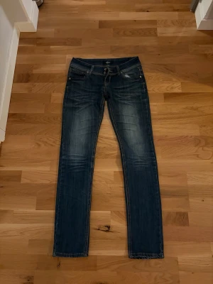 Mörkblå skinny jeans från Soulwear - Säljer ett par mörkblå skinny jeans från Soulwear med snygga slitningar och dubbla knappar i midjan. Klassisk femficksmodell och kontrastsömmar. Jeansen har låg midja och är tillverkade i stretchig denim för skön passform.