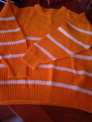 Randig orange stickad tröja - Säljer en ribbstickad tröja i bomull. Den är vackert gul färg med vita horisontella ränder. Tröjan har rund halsringning, långa ärmar och breda muddar vid ärmslut och nederkant. Perfekt för dig som gillar färg och vill ha en mysig, casual vibe.