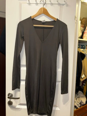 Mörkgrå ribbad klänning från Gina Tricot - Säljer en mörkgrå, ribbad och figurnära klänning från Gina Tricot i storlek XS. Klänningen har lång ärm, v-ringning och är i kort modell. Perfekt för dig som gillar en enkel men stilren look.