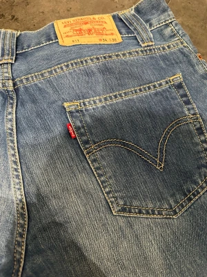 Levi's 511 blå jeans W34 L30 - Säljer ett par klassiska Levi's 511 jeans i blå tvätt. De har raka ben, fem fickor och den ikoniska röda Levi's-lappen på bakfickan. Jeansen har gul kontrastsöm och dragkedja i gylfen. Perfekta för dig som gillar tidlös denimstil.