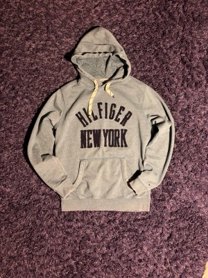 Hilfiger hoodie - Säljer en fet hilfiger hoodie med vintage känslan och flera coola detaljer. Den är skön och har en färg som kan få outfiten att sticka ut. Notera att färgen är lite mörkare än vad den ser ut att vara på bilderna, annars inga defekter. Hör av er vid minsta fundering!
