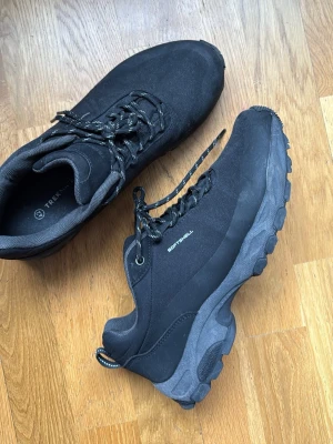 Svarta skor  - Svarta trekkingskor från Trekmates med grov sula och snörning. Skorna är tillverkade i softshell-material och har en sportig look med diskreta reflexdetaljer på hälen. Perfekta för utomhusaktiviteter och äventyr.