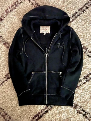 True religion zip hoodie - Säljer min True religion zip som jag knappt använt, denhär i storlek S men passar bra som M och i 10/10 skick, den är köpt på NK vartifrån jag har kvitto och tags kvar, se bild 4 å 5. Har inte fått så mycket användning av den för den var lite liten på mig som är 194. Kom gärna med frågor, Pris går att diskutera 