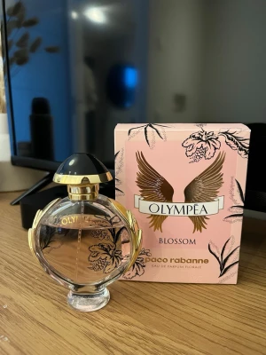 Olympea Blossom EdP 50ml - Olympea Blossom från Paco Rabanne är en Eau de Parfum Florale i en snygg rosa flaska med gulddetaljer. 50ml, perfekt att ta med i väskan. Fräsch och modern design som sticker ut på hyllan. Lite använd, syns på bilderna hur mycket som är kvar!💗
