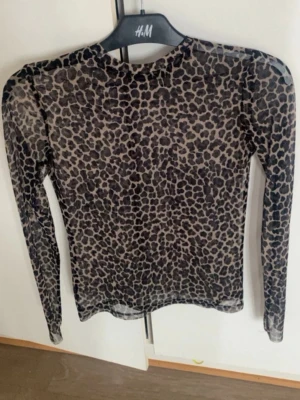 Leopardmönstrad mesh topp från H&M - Säljer en transparent långärmad mesh topp från H&M med leopardmönster i svart och beige. Tight passform och rund halsringning, perfekt att styla lager på lager eller till ett par jeans.