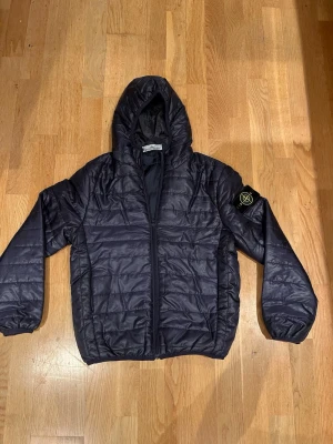 Svart pufferjacka från Stone Island - Säljer en svart pufferjacka från Stone Island med huva och dragkedja framtill. Jackan är i storlek M men passar bättre för dig som har storlek S. MVH / Olle 