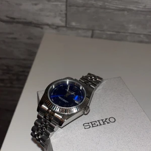 Seiko mod automatik  - Automatisk Seiko-mod i djupt blått med karaktäristiska arabiska tecken. En klocka som verkligen sticker ut på handleden. Samt är det safirglas 