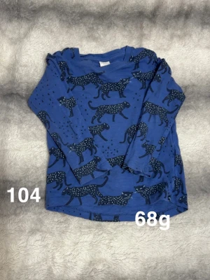 Blå långärmad topp med leopardmönster - Säljer en blå långärmad topp med coolt leopardmönster i mörkblått och vita prickar. Toppen har rund hals, perfekt för dig som gillar djurprint och vill ha något bekvämt och snyggt.🌸 Fint använt skick. Storlek 104