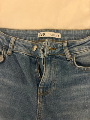 Blå bootcut jeans från Zara - Säljer ett par ljusblå bootcut jeans från Zara med klassisk femficksdesign och dragkedja. Jeansen har låg midja och är tillverkade i mjukt denimtyg av bomull. Perfekta för dig som gillar en retroinspirerad look med utsvängda ben.