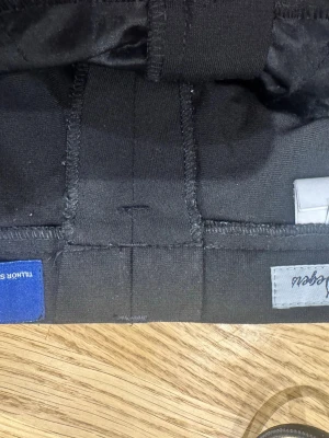 Svarta kostymbyxor från Oscar Jacobson - Säljer ett par klassiska svarta kostymbyxor från Oscar Jacobson. Byxorna har raka ben, bälteshällor och stängs med hake och dragkedja. Materialet är mjukt och känns som en blandning av bomull och polyester. Perfekta till en stilren look.