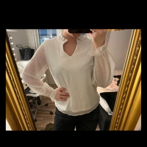 Vit blus med volangkrage och prickar - Säljer en söt vit blus med diskret prickigt mönster, volangdetaljer vid halsringningen och ärmsluten samt v-ringning. 