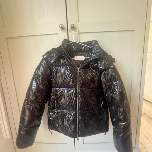 Svart glansig pufferjacka från Nelly XS - Svart pufferjacka från Nelly i glansigt material med dragkedja. Jackan har en fin passform och är perfekt för kalla dagar. Snygg och trendig look som sticker ut med sin blanka finish. Luvan går även och ta bort. Nästan aldrig används så är som ny. Ny pris är 799 men säljer för 399. Pris kan diskuteras inom nära summa🩷