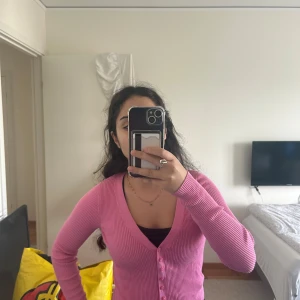 Rosa ribbad kofta från Pimkie - Säljer en söt rosa kofta från Pimkie med ribbad struktur och v-ringning. Koftan har långa ärmar, knappar framtill och sitter snyggt figurnära. Perfekt att slänga över ett linne eller t-shirt för en chill look.