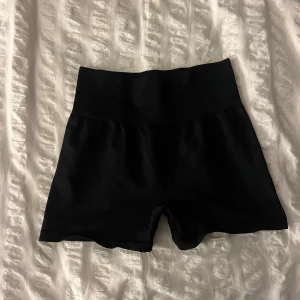 Svarta träningsshorts H&M Move - Svarta, tighta och högmidjade träningsshorts från H&M Move. De är tillverkade i ett stretchigt syntetmaterial med ribbad struktur och sitter skönt mot kroppen. Perfekta för gymmet eller löprundan. Snygg och enkel design som funkar till allt.